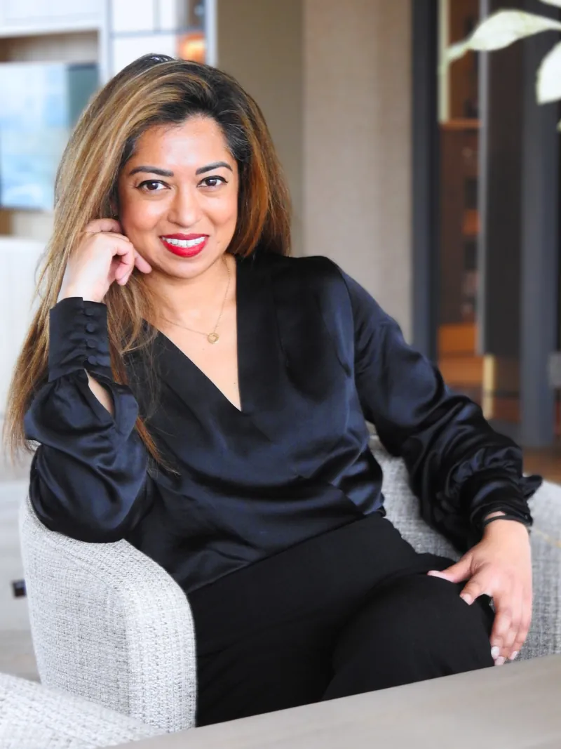 Astrid Karim, lachend in een fauteuil met haar hand tegen haar wang